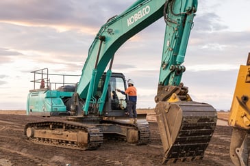 man standing on green kobota excavator 
