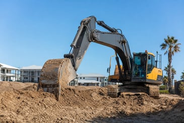 Medium excavator digging on a Sunshine Coast subdivision with houses and palm trees in the background.