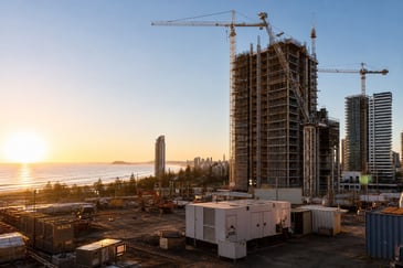 High-rise Gold Coast construction site near the beach with mobile generators powering cranes and site sheds at sunrise.