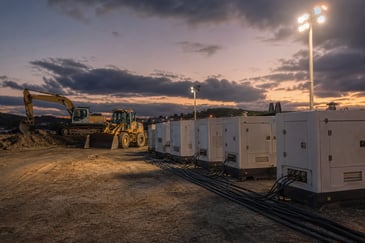 Industrial generators powering floodlights beside earthmoving equipment on a Central Coast construction site at dusk.