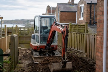 Mini excavator working in a tight residential Newcastle backyard near brick houses.