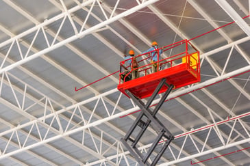 Electric scissor lift with a worker at height inside a Sydney warehouse fit-out.